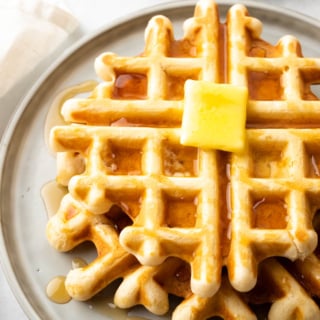 Nahaufnahme eines Stapels natriumarmer Waffeln auf einem grauen Teller, bedeckt mit Sirup und einem Stück Butter darüber