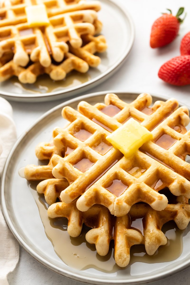 Nahaufnahme eines Stapels natriumarmer Waffeln auf einem grauen Teller, bedeckt mit Sirup und einem Stück Butter darüber