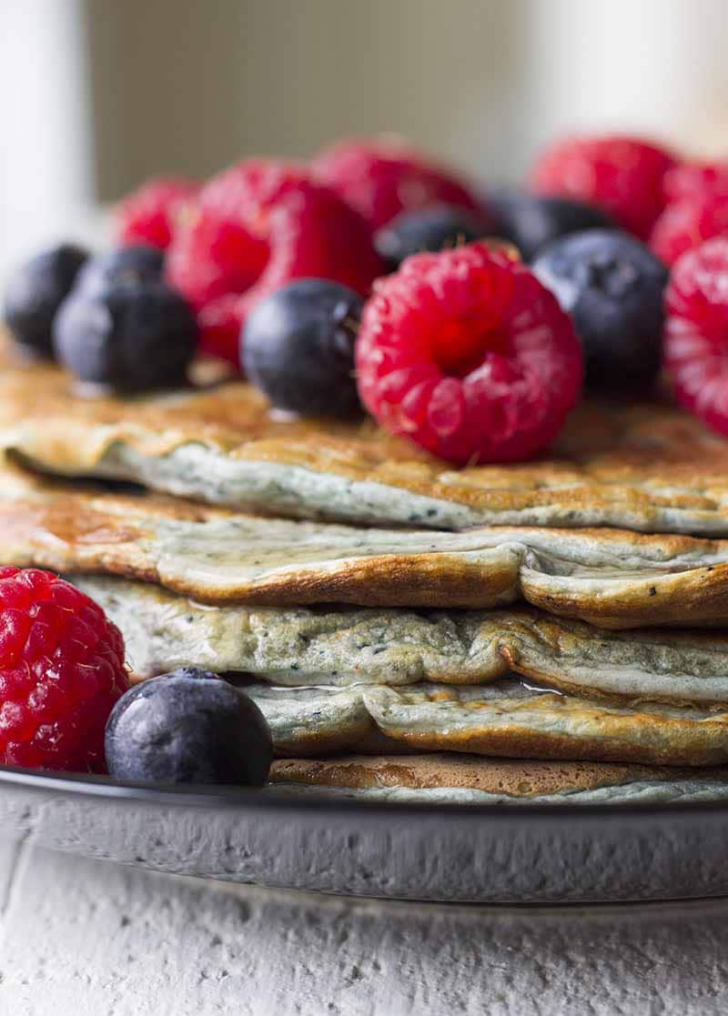 Ein Stapel Proteinpfannkuchen auf einem schwarzen Teller mit gemischten Beeren darauf.