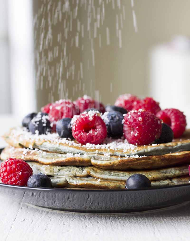 Stevia über einen Stapel Pfannkuchen mit Beeren und zuckerfreiem Sirup streuen